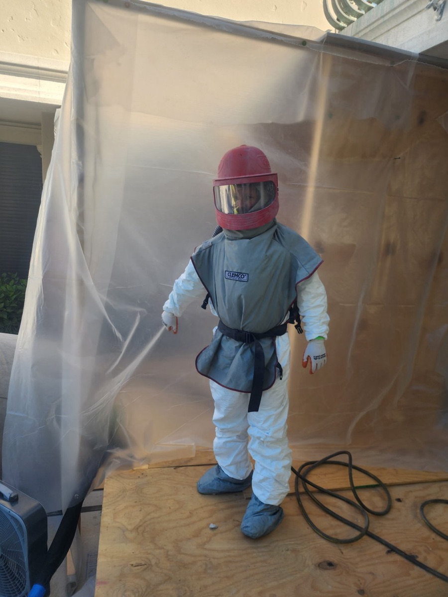 SWFL Media Blasters technician in full containment gear inside a plastic-draped work enclosure