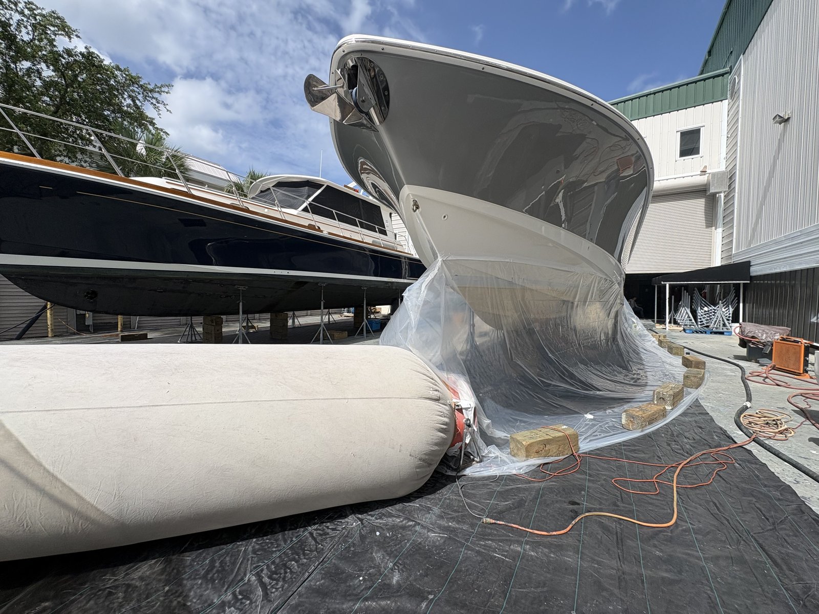 Motor yacht bow at a Southwest Florida boatyard, hull masked and wrapped for bottom work